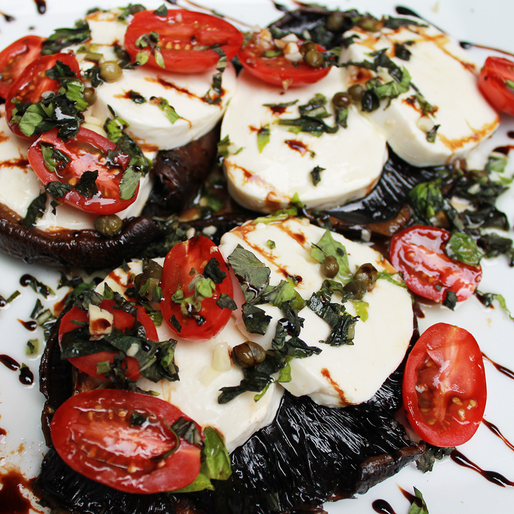 Roasted portobello mushroom caps topped with thick slices of fresh mozzarella cheese, halved cherry tomatoes, chopped basil, capers, and a balsamic glaze.
